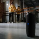 a man in yellow hoodie looking at the wireless speaker on the floor